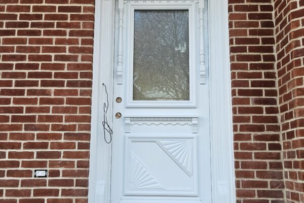 Porte d'entrée blanche sur mur en briques rouges.