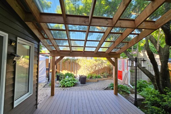 Terrasse bois avec toit transparent et jardin verdoyant.