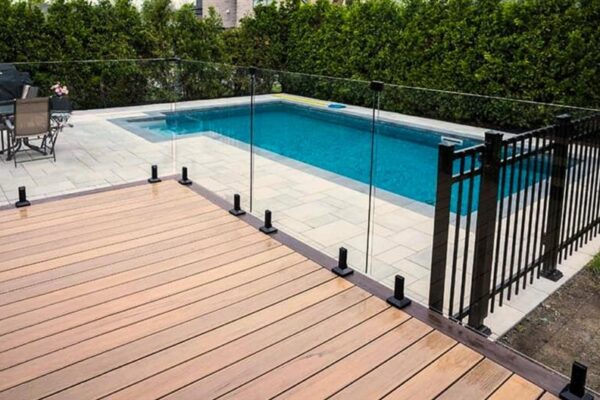 Piscine extérieure avec terrasse en bois et clôture.
